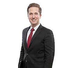 Schneider Felix stehend mit dunklem Sakko und roter Krawatte