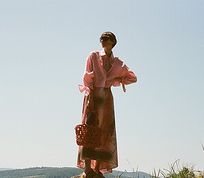 Frau mit lachsfarbenen, gemusterten Kleid in der Natur.