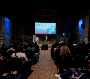 Vortragssaal mit Speakern, Publikum und Bildschirm "Numix Lab"