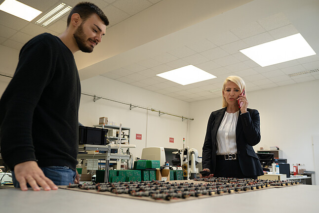 Ulrike Haslauer und ein Mitarbeiter von Compact Electric betrachten elektronische Bauteile auf einem Tisch in der Entwicklungsabteilung des Unternehmens.