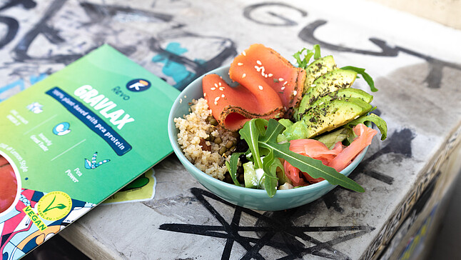 Revo Foods: Auf einem Tisch liegt eine Packung Gravlax von Revo Foods und eine Lachsbowl mit Avocado, Salat und Couscous.