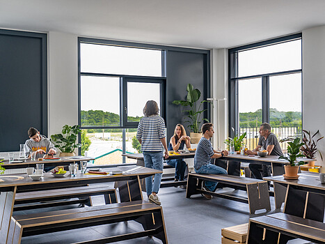 Eine Gruppe Menschen in einem Aufenthaltsraum. Sie essen und unterhalten sich